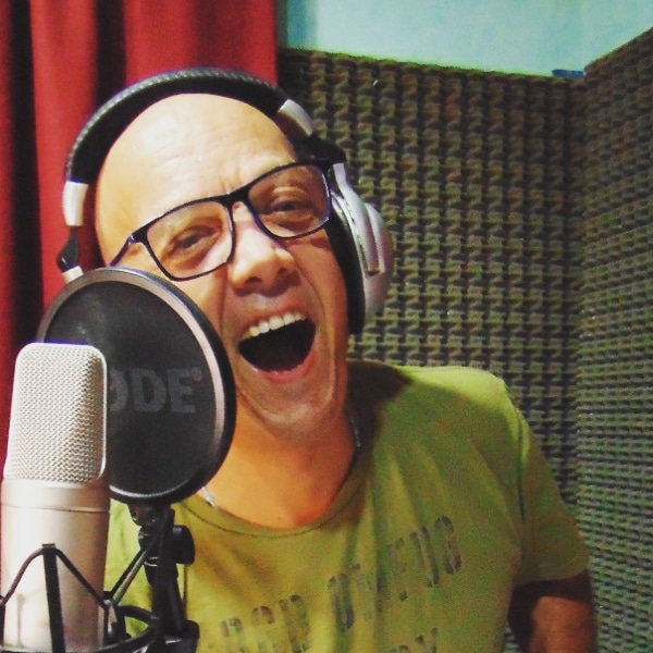 Hombre dentro de un estudio de radio sonriendo frente al micrófono y usando auriculares